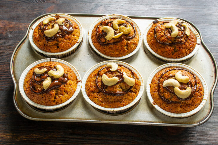 Decorate warm muffins with melted chocolate and cashews for a final touch Freshly baked coffee banana muffins on a wire rack, being decorated with melted chocolate.