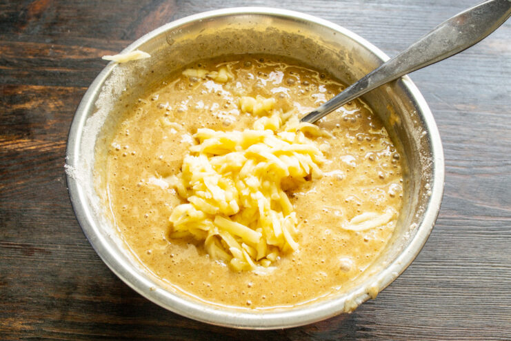Adding grated banana to the batter for natural sweetness and moisture Adding freshly grated banana to the coffee muffin batter in a bowl.