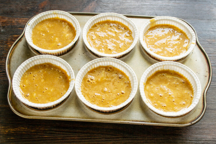 Fill paper liners in a muffin tin about two-thirds full for a perfect rise Scooping muffin batter into colorful paper liners in a muffin tin.