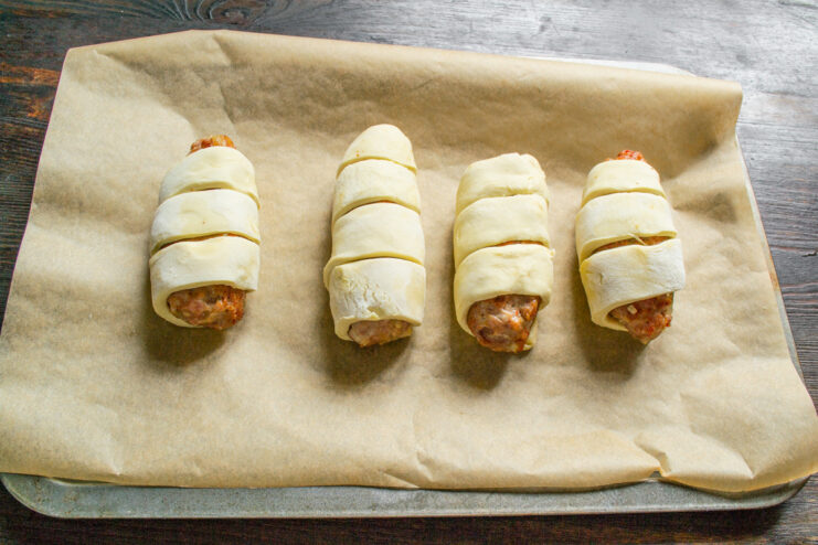 Pastry-wrapped meat patties arranged on a baking sheet lined with parchment paper.