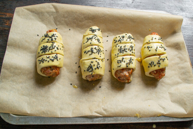 Black sesame seeds being sprinkled over the egg-washed pastry-wrapped patties.