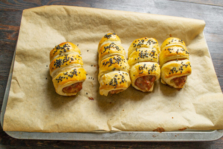 A baking sheet with meat patties in pastry being placed into a hot oven.