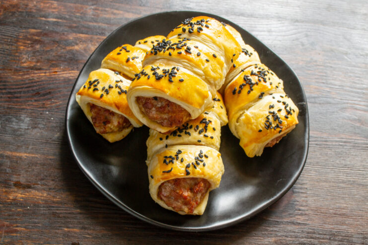 A close-up of golden-brown, freshly baked meat patties in pastry on a plate.
