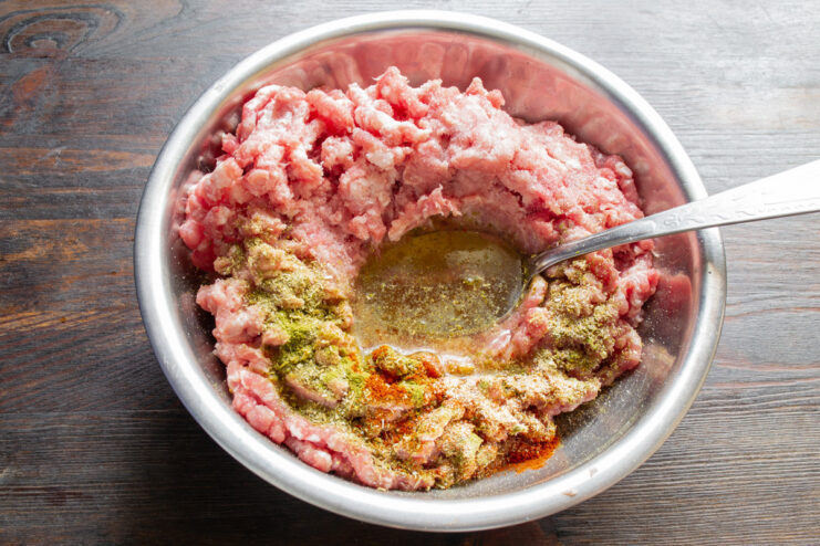 Cold chicken broth being poured into a bowl of ground meat.