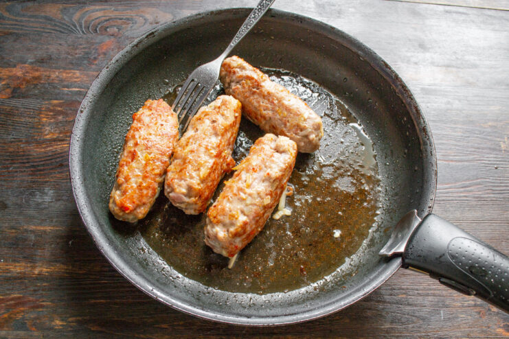 Meat patties being seared in a hot skillet until golden brown.