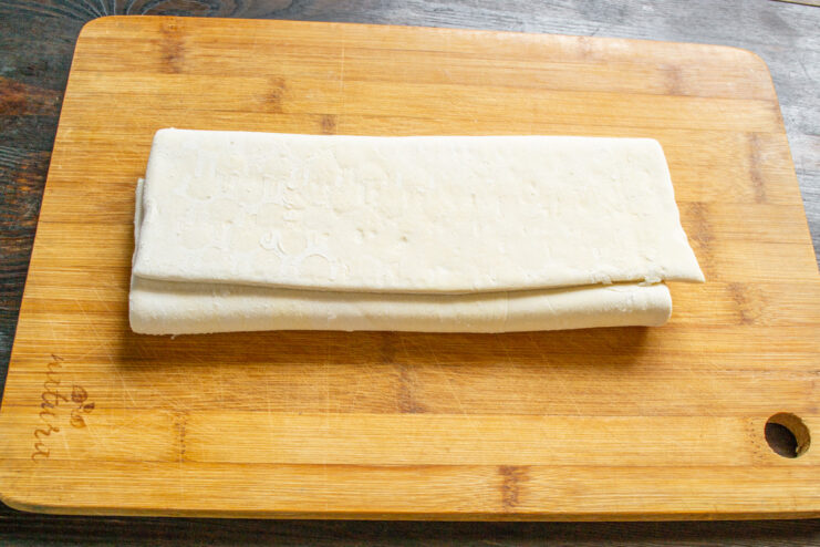 A sheet of frozen puff pastry thawing on a floured surface.