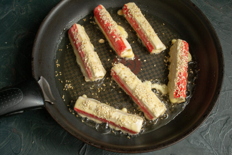 Battered crab sticks frying in hot oil in a pan, turning golden brown.