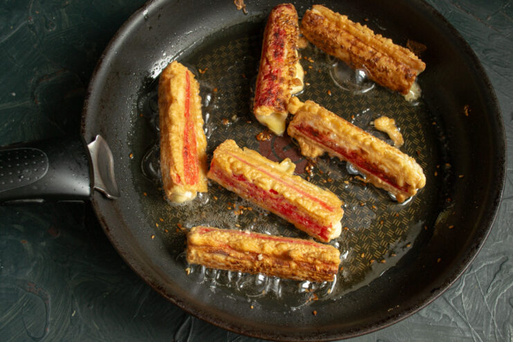 Golden-brown crab sticks being flipped in a frying pan.
