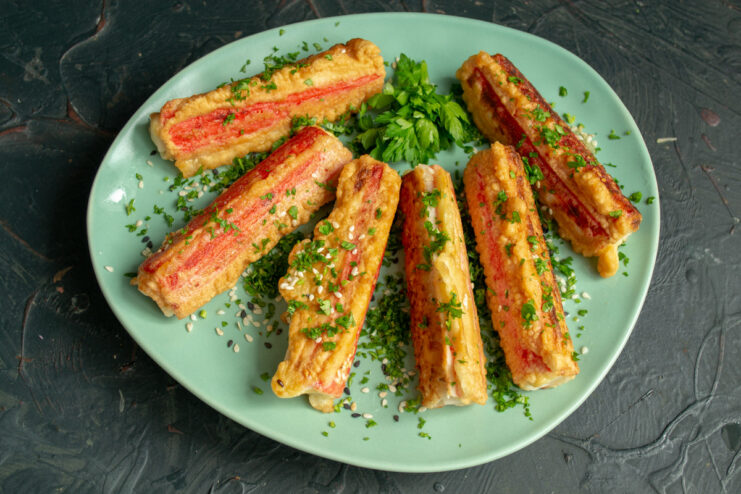Finished fried crab sticks on a plate, garnished with herbs and sesame seeds, ready to serve.