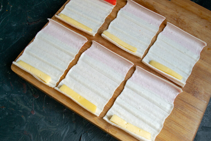 A hand placing a stick of cheese onto an unrolled crab stick sheet.