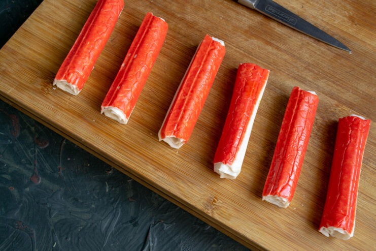 A crab stick being carefully rolled up with a cheese stick inside.