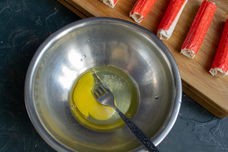 An egg being whisked with a fork in a white bowl to make the batter.
