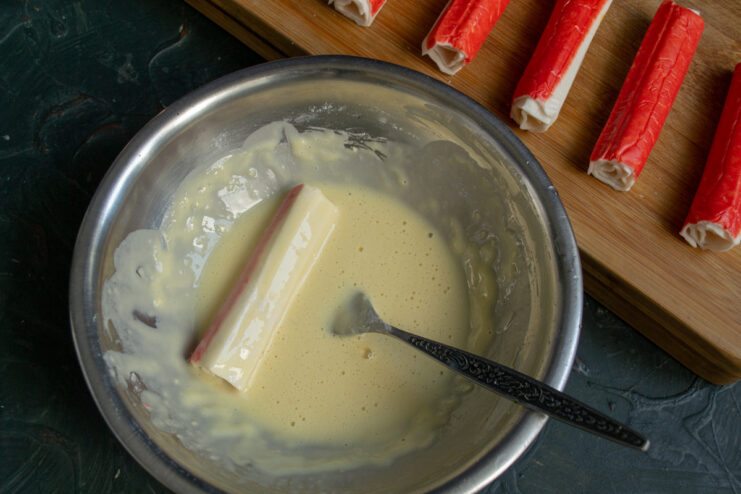 A cheese-stuffed crab stick being dipped into a bowl of batter.