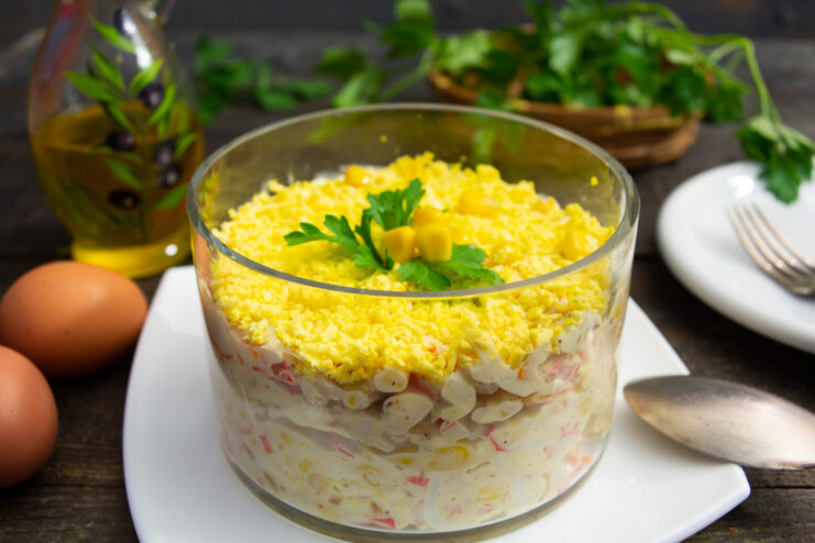A bowl of finished imitation crab salad with corn and processed cheese, garnished with herbs.