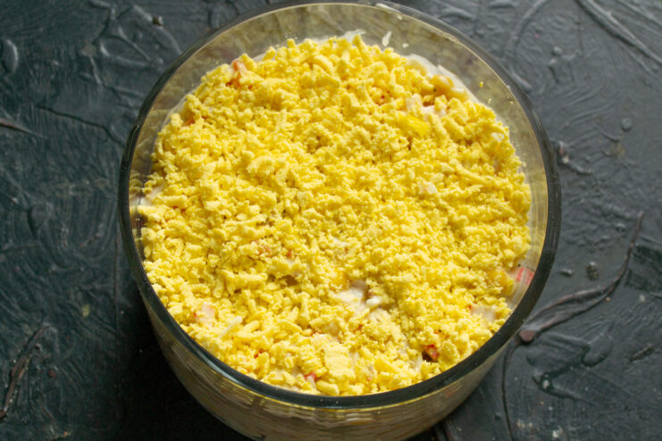 Grating Egg Yolks for a Beautiful and Flavorful Garnish A hand grating a hard-boiled egg yolk over the salad using a fine grater.