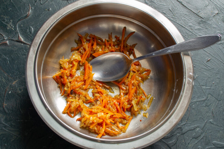 Cooling the Sautéed Vegetables Before Mixing the Salad Sautéed onions and carrots in a white bowl, cooling down.