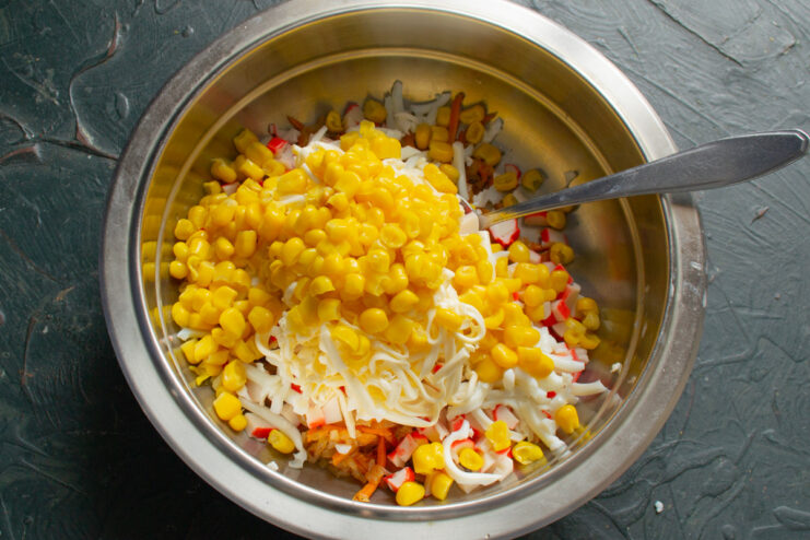 Adding Sweet Canned Corn to the Salad Mix Canned corn being added to a bowl with crab sticks and vegetables.