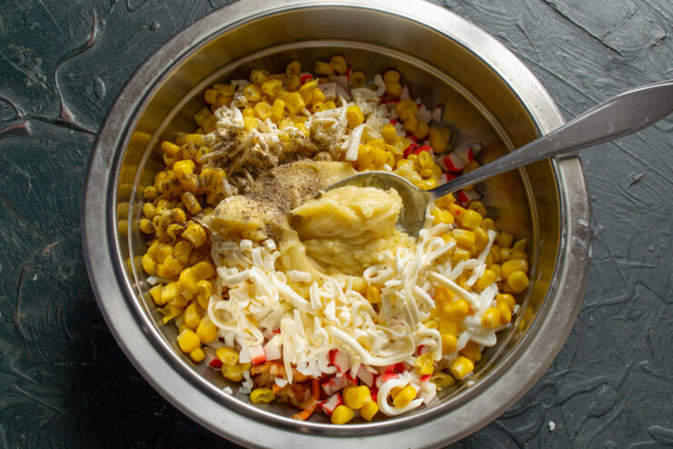Dressing the Salad with Creamy Homemade Mayonnaise A spoonful of homemade mayonnaise being added to the salad ingredients in a bowl.