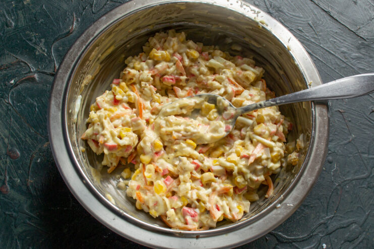 Mixing All the Salad Ingredients Together Until Well Combined Mixing the imitation crab salad with a spoon in a large bowl.