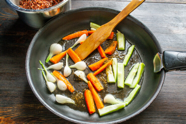 Sautéing fresh vegetables in olive oil for the rice dish. Chopped carrots, zucchini, and onions being added to a hot frying pan with oil.