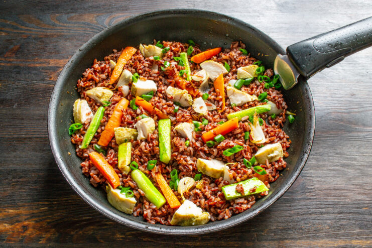 Finishing the dish by adding cooked chicken. Chopped cooked chicken breast being added to the pan with red rice and vegetables.