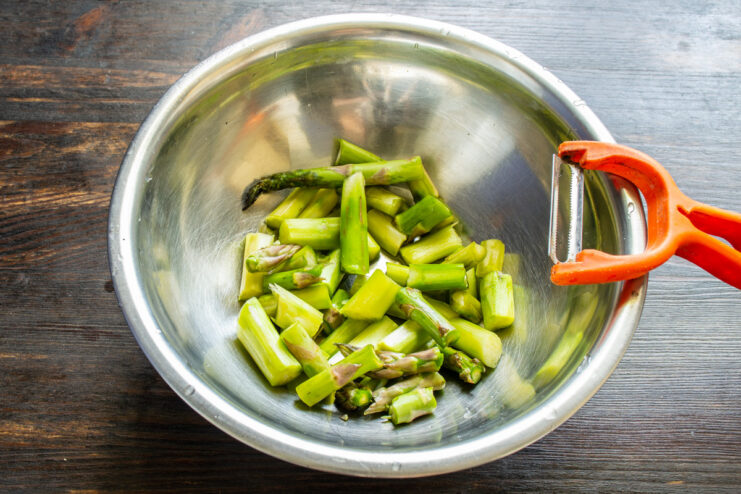 How to properly trim and prepare fresh asparagus stalks for the soup. Fresh green asparagus stalks being trimmed on a cutting board.