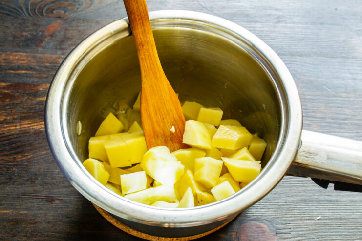 Cubing potatoes to add creaminess and body to the soup. Peeled potatoes being diced into small, even cubes on a cutting board.