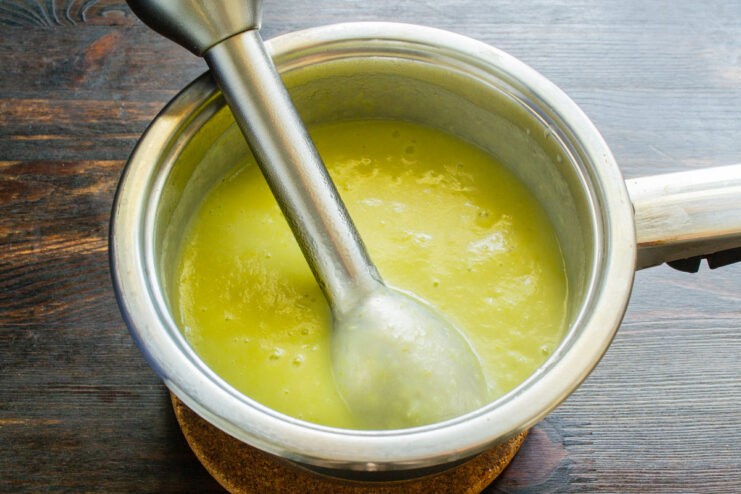 Using an immersion blender to create a smooth, creamy soup texture. An immersion blender pureeing the asparagus soup directly in the saucepan.
