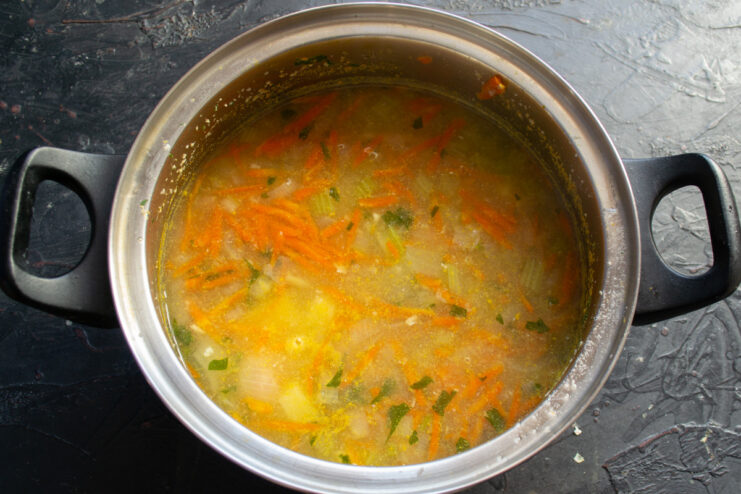 A covered pot simmering on a stove, cooking the vegetable soup base.