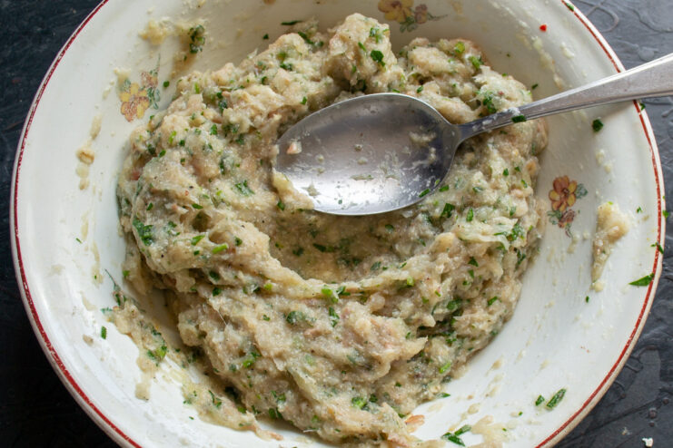 Ingredients for fish meatballs in a bowl: minced fish, egg, and herbs.