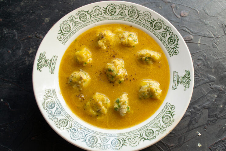 A ladle pouring creamy fish soup with meatballs into a white bowl.
