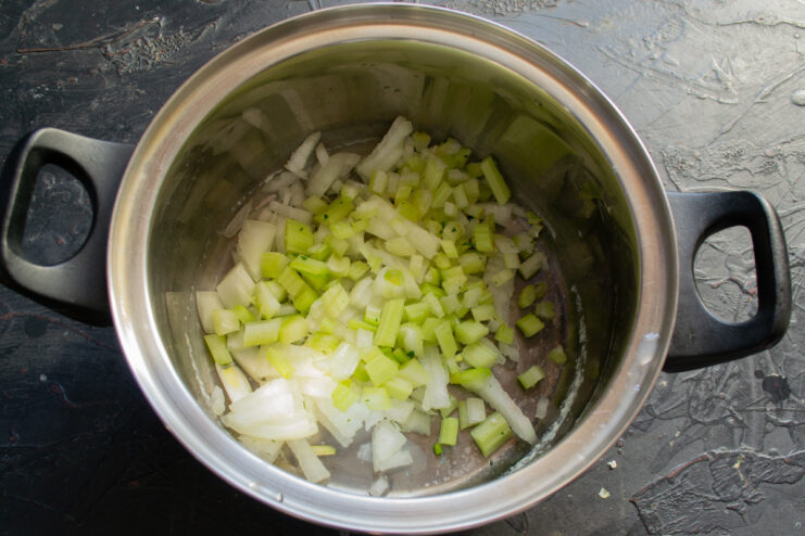 A hand holding a knife, finely chopping a yellow onion on a cutting board.