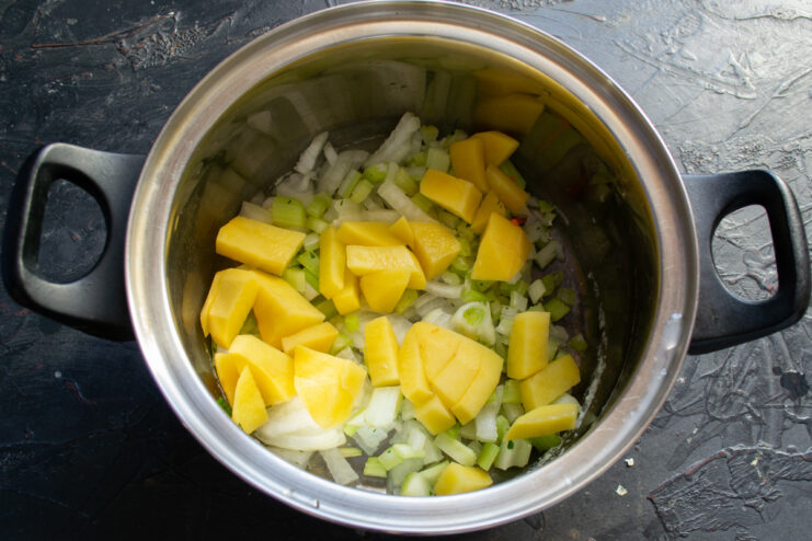 Diced potatoes being added to a pot containing chopped onions and celery.