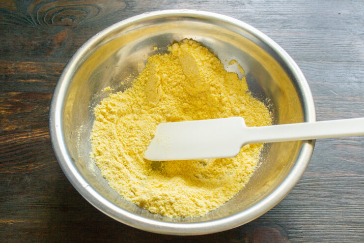 Preparing the Dry Ingredients for Corn Fritters A bowl with cornmeal and baking powder being mixed for the fritter batter.
