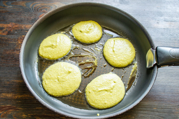 Frying the Corn Fritters to a Golden Brown Corn fritters cooking in a hot frying pan, one side golden brown.