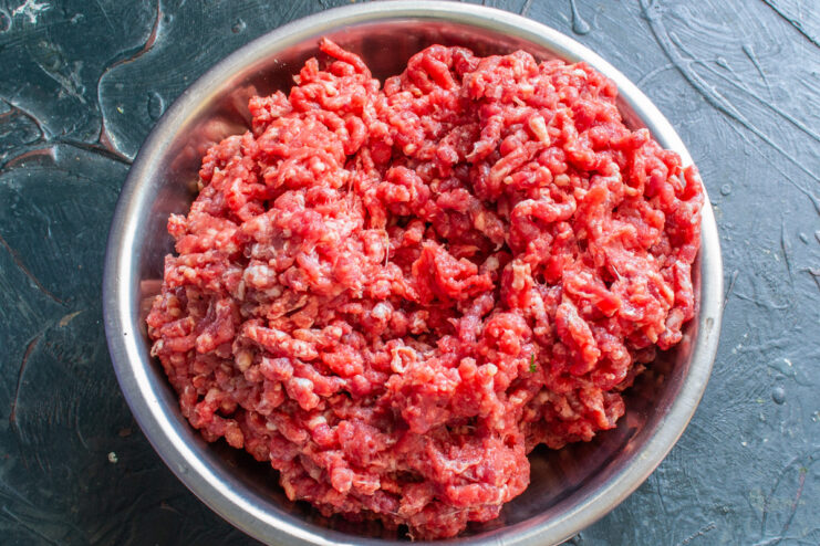 Step 1: Grinding the Beef for Kupaty Sausages Close-up of beef being ground in a meat grinder for making sausages.
