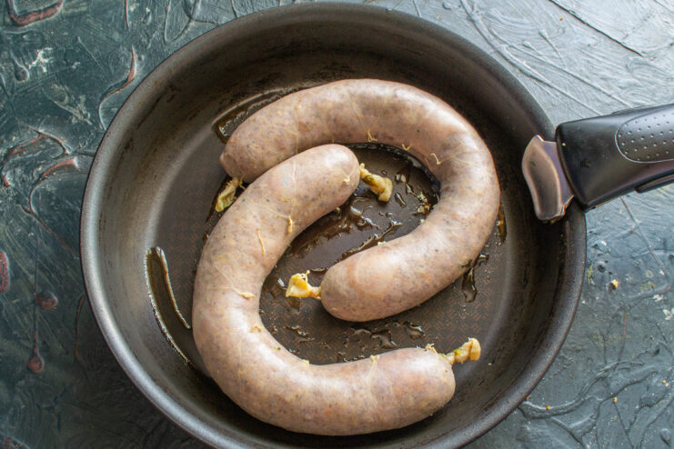 Frying Homemade Kupaty to a Golden-Brown Perfection Beef kupaty sausages sizzling in a hot frying pan, being cooked until golden brown.