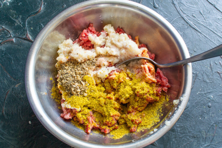 Step 4: Seasoning the Beef Mixture for Kupaty Spices, including crushed coriander and curry powder, being added to the ground beef mixture in a bowl.