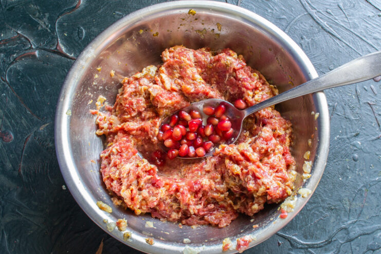 Step 5: Mixing the Sausage Filling and Adding Pomegranate Hand mixing ground meat with pomegranate seeds in a bowl to create the sausage filling.