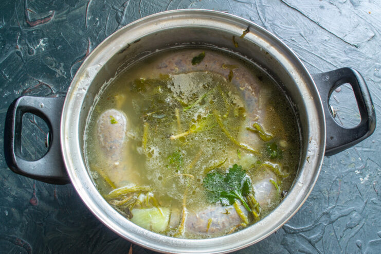 Parboiling the Kupaty Sausages Before Frying or Grilling Kupaty sausages being placed into a pot of boiling water with tongs.