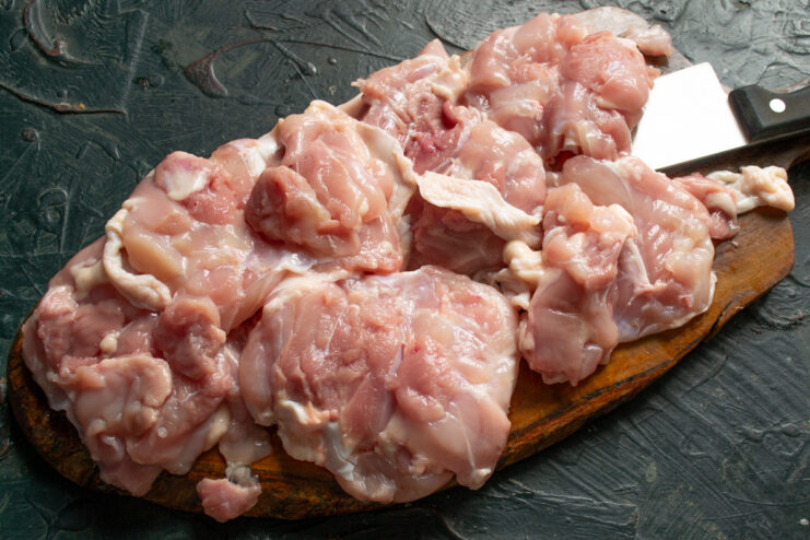 How to Debone Chicken Thighs for Even Cooking A person deboning a raw chicken thigh on a cutting board with a sharp knife.