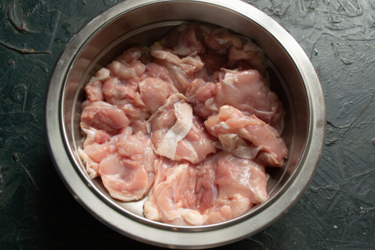 Marinating Chicken in Wine for Extra Flavor Raw chicken thighs in a bowl being marinated with white wine.