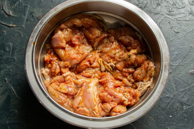 Ensuring Every Piece of Chicken is Coated in Marinade Mixing chicken thighs with marinade and spices in a white bowl.