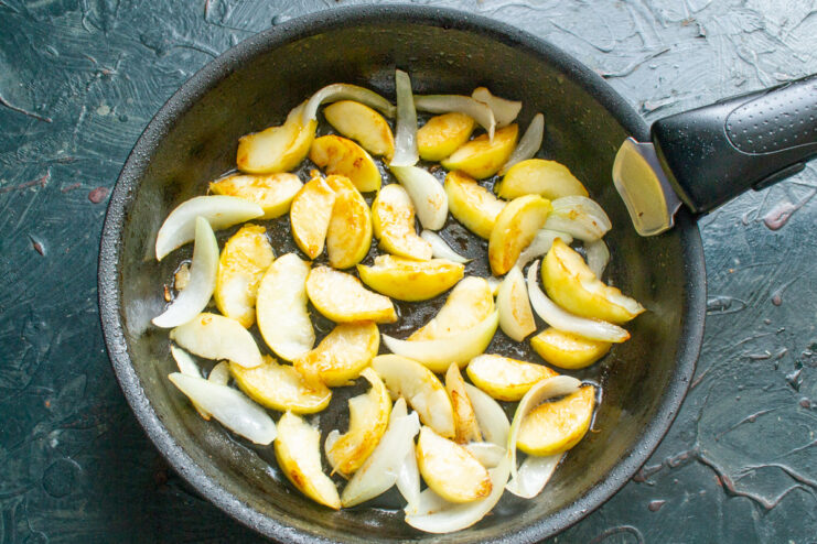 Caramelizing the apples brings out their natural sweetness. Apple slices and onions caramelizing in a skillet.