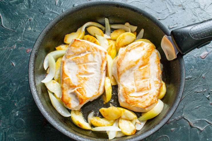Combining the chicken with the sautéed apples and onions. Seared chicken breasts being placed back into the skillet with cooked apples and onions.