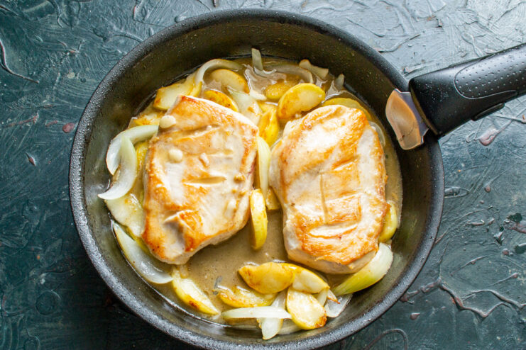 Adding the tangy honey-mustard sauce to the pan. Honey-mustard sauce being poured over chicken and apples in a skillet.