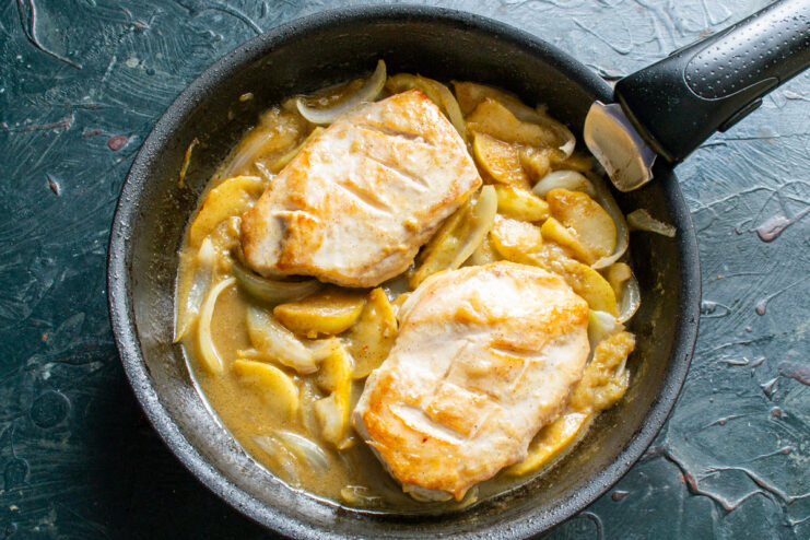 Simmering everything together to let the flavors meld. Chicken and apples simmering in the honey-mustard sauce in a skillet.