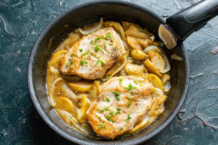 Garnishing the finished dish with fresh herbs before serving. The finished chicken and apple dish in a skillet, garnished with fresh parsley.