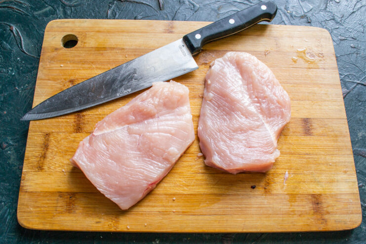 Step 1: Preparing the chicken breast fillets. Two raw chicken breast fillets on a wooden cutting board.