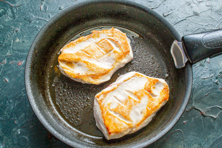 Setting the seared chicken aside while preparing the sauce base. Golden-brown seared chicken fillets being removed from a skillet.